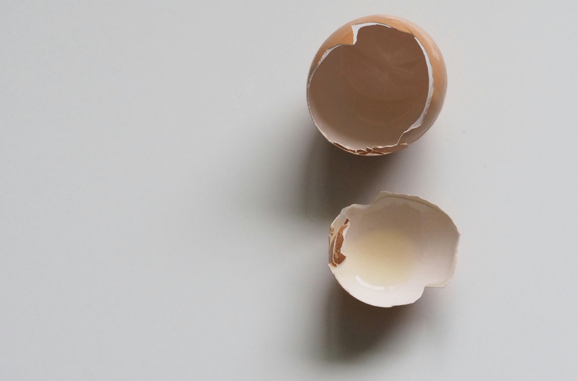Two halves of an egg shell, arranged on a surface so that their emoty insides show towards the camera above them.